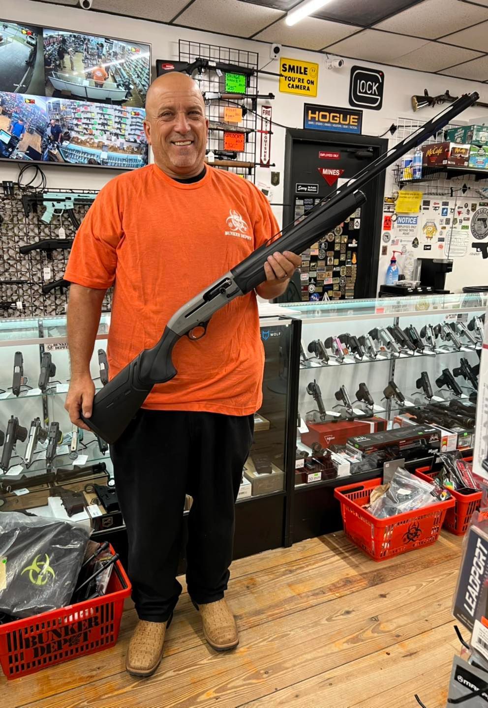 A guy in an orange shirt is holding a rifle inside the gun store.
