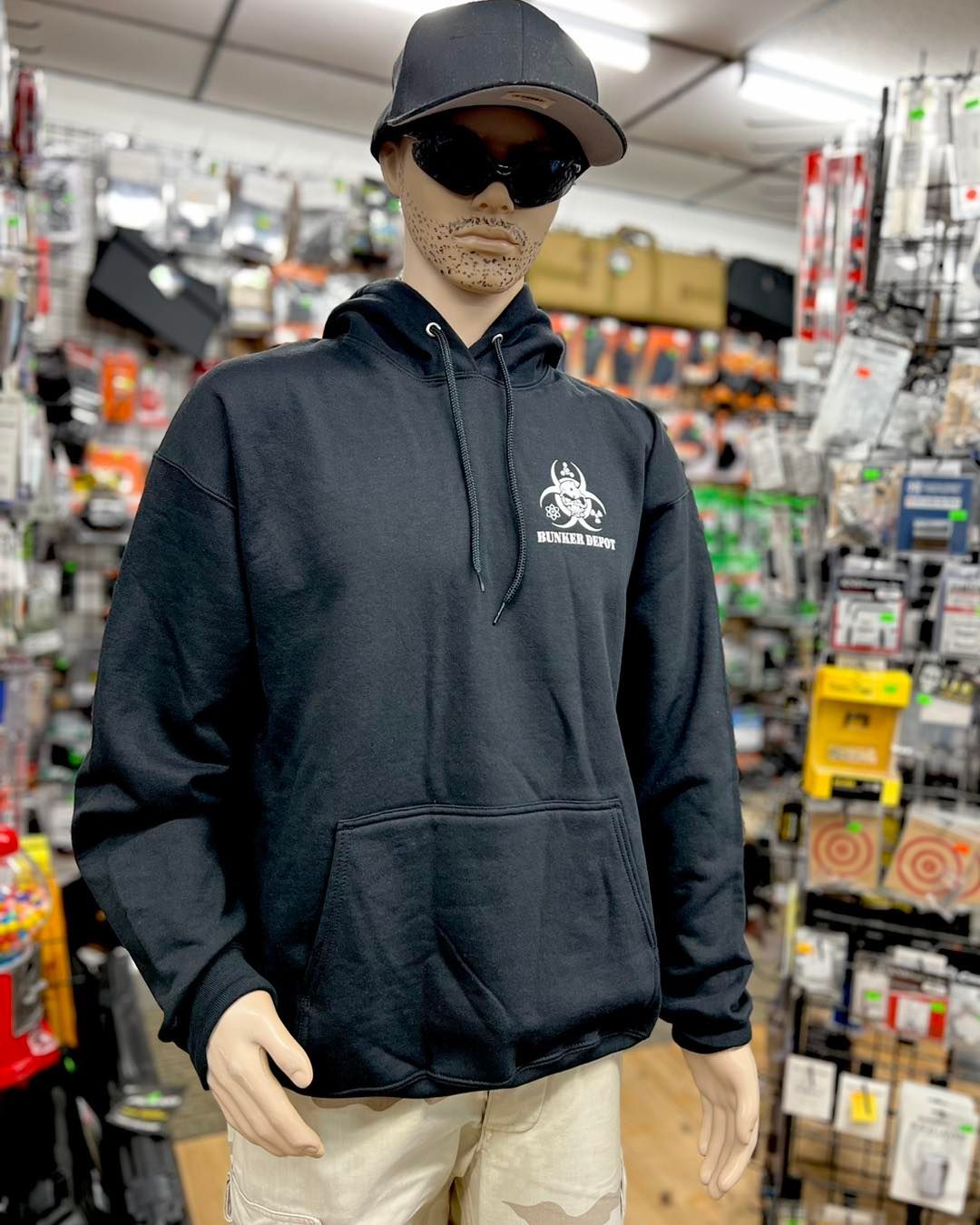 A mannequin wearing a black hoodie and sunglasses is standing in a store.
