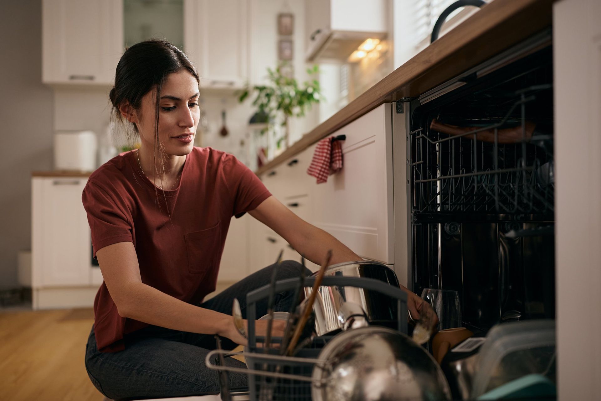 Woman loading dishes into an open dishwasher in a bright kitchen