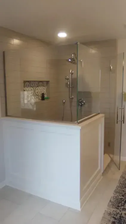 Corner shower with glass doors, white tiled walls and base, shower fixtures, and built-in shelf.
