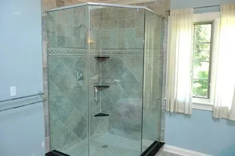 Glass-doored shower in blue-tiled bathroom, with window and white curtains, showcasing tiled interior.