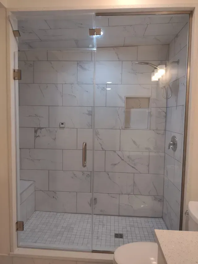 Glass-door shower with white marble-look tiles, a built-in bench, and a rectangular niche.