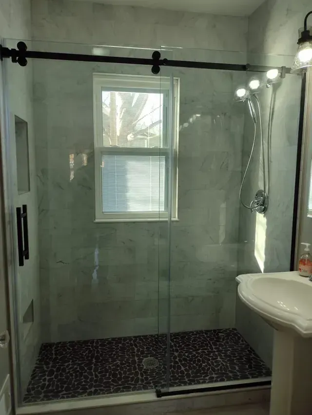 Modern bathroom with a glass shower, marble tile, black hardware, and a small window.