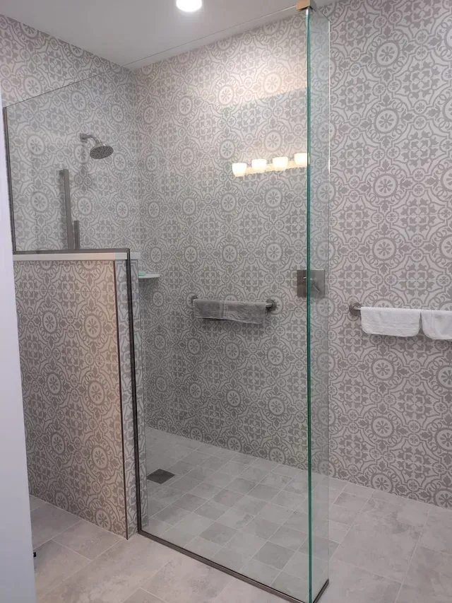 A modern bathroom with a glass shower enclosure. Gray patterned tiles cover the walls and floor.