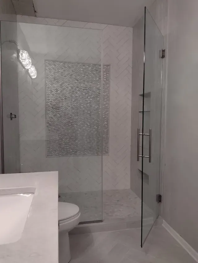 Modern bathroom with glass shower door, mosaic tile accent, white sink and toilet.
