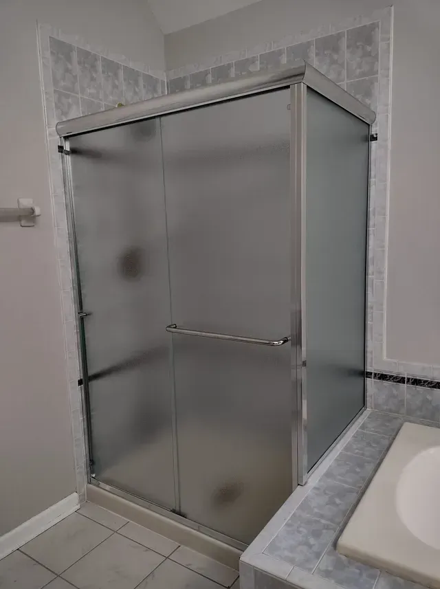 Frosted glass shower enclosure with silver frame, adjacent to a countertop and tiled walls.