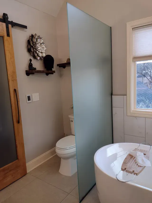 Bathroom with frosted glass panel, toilet, and freestanding tub; wooden door and shelves.