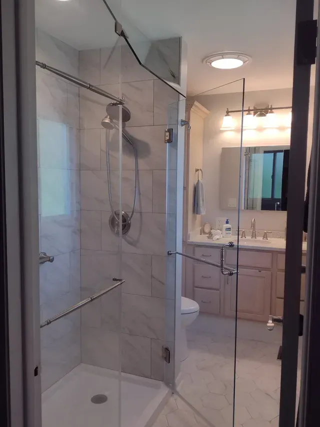 Modern bathroom with glass shower, white tile, and vanity.