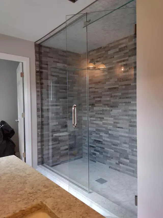 Glass shower enclosure with gray tile walls and chrome fixtures.