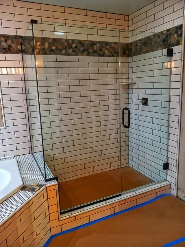 Glass shower enclosure with white brick tile walls and a decorative stone border.