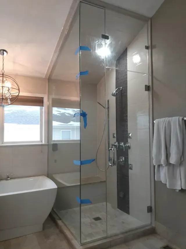Glass shower enclosure in a bathroom with a tub, window, and towel rack.