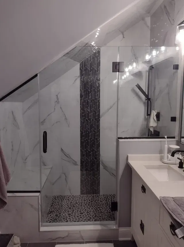 Angled glass shower with black fixtures and white marble tile in a bathroom.