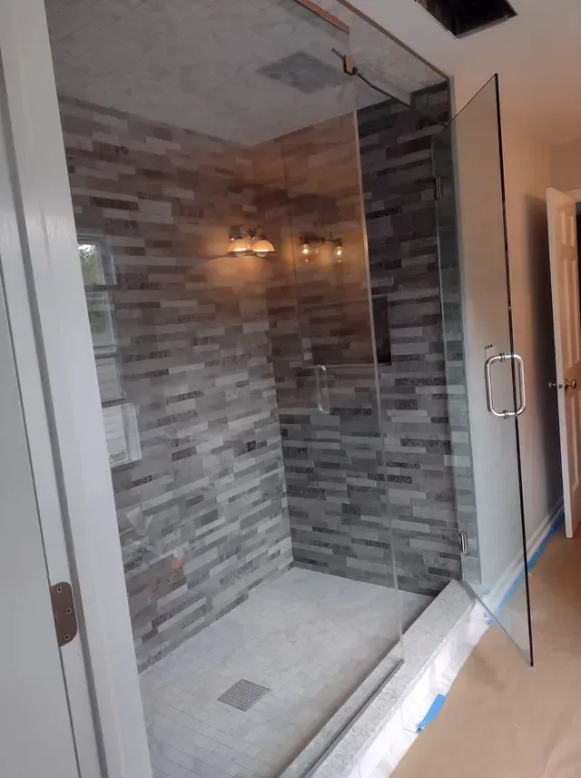 Modern shower with gray stone-like tiles, glass door, and chrome fixtures.