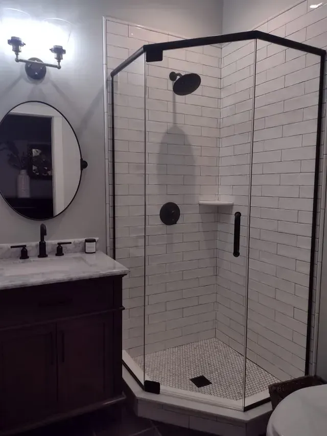 Bathroom with dark vanity, black-framed shower, white subway tiles, round mirror, and black fixtures.