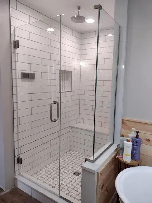 Glass-enclosed shower with white subway tile, a built-in bench, and a round shower head.