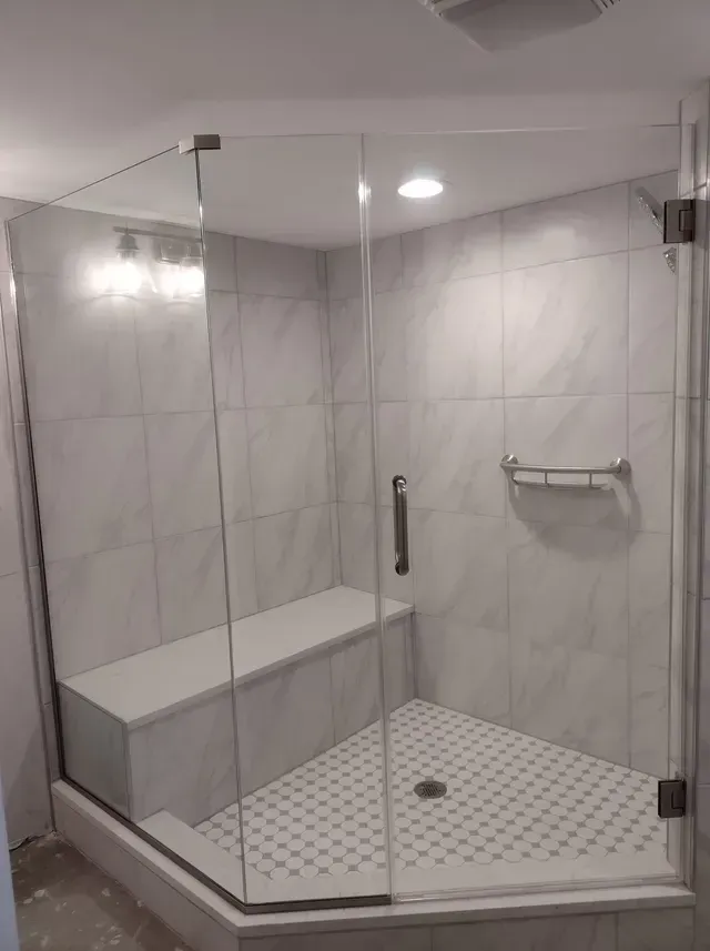 Tiled, corner shower with glass doors, a built-in seat, and a grab bar; white and gray.