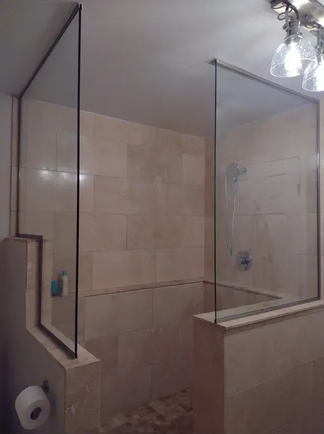 Shower with glass panels and beige tile walls. Toilet paper roll is visible.