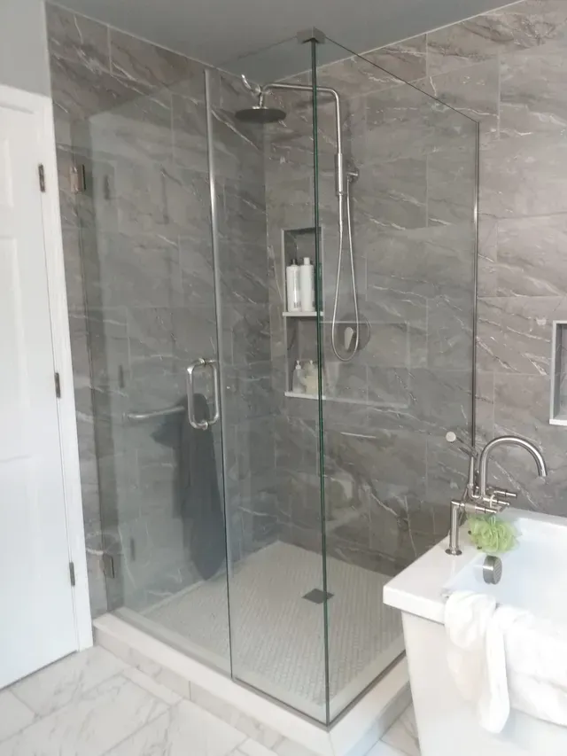 Modern bathroom with gray tiled shower and glass door. White tub and floor.