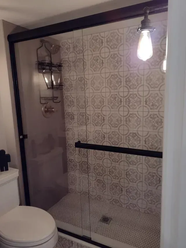 Shower with patterned tile, glass doors, black frame, and a hanging light.