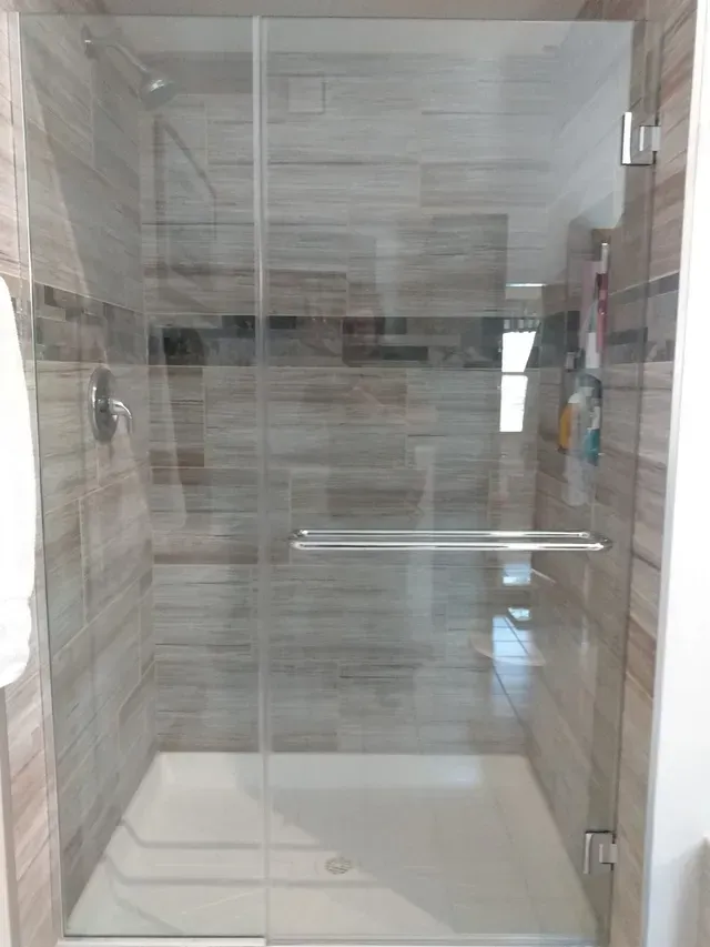 Glass shower with chrome fixtures and brown tiled walls.