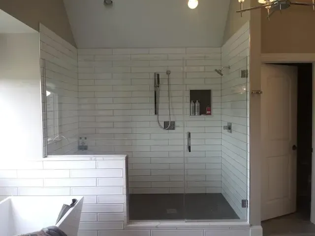 A modern bathroom with white subway tile shower, glass doors, and gray floor.
