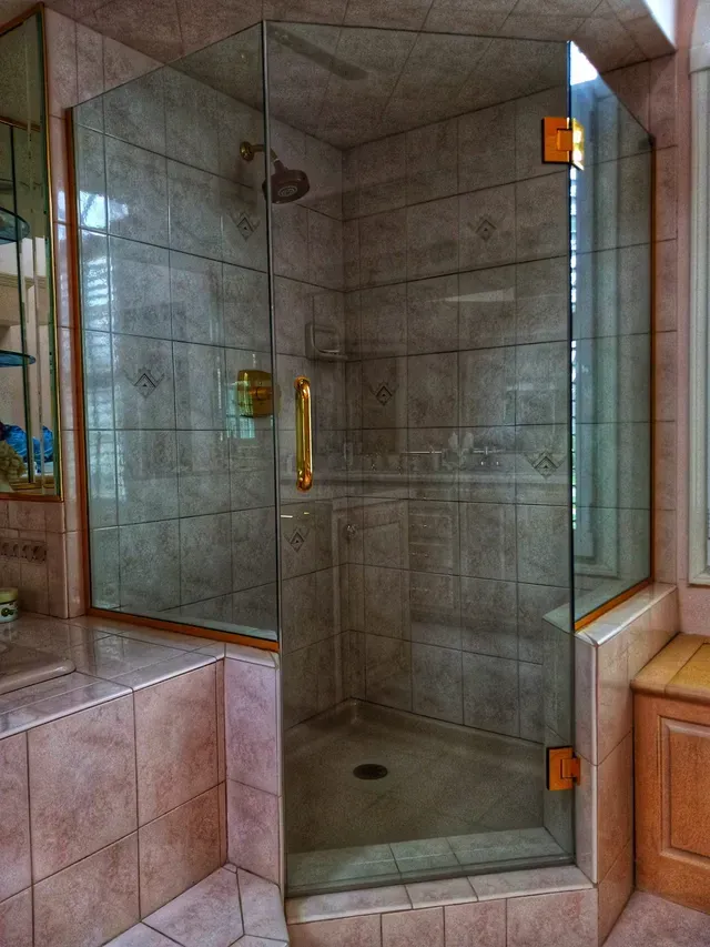 Glass shower enclosure with gold hardware, tan tile walls.