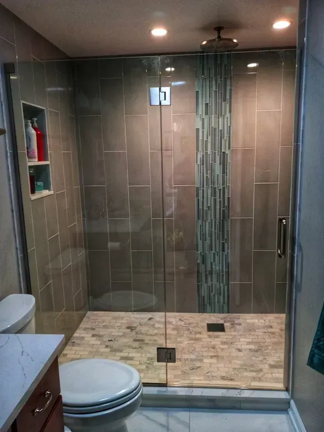 Modern bathroom with glass shower doors, gray tile walls, and a mosaic tile accent strip.