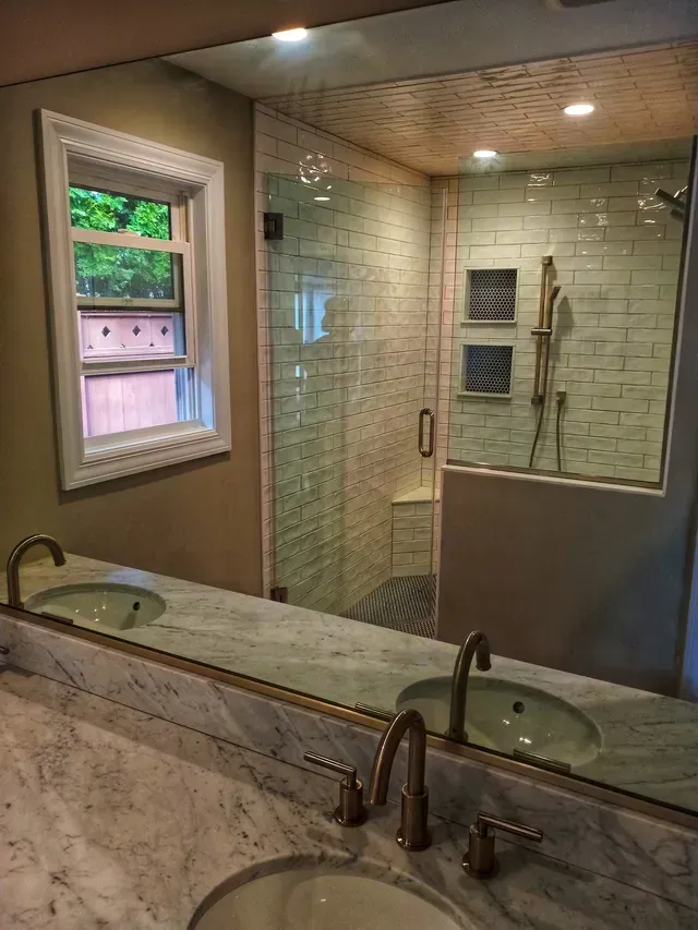 Bathroom with marble vanity, framed mirror, glass shower, and small window.