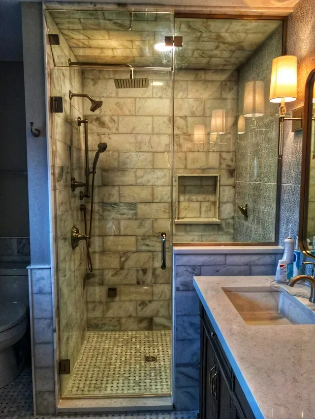 Bathroom with marble tile shower, glass door, and sink with dark cabinets.