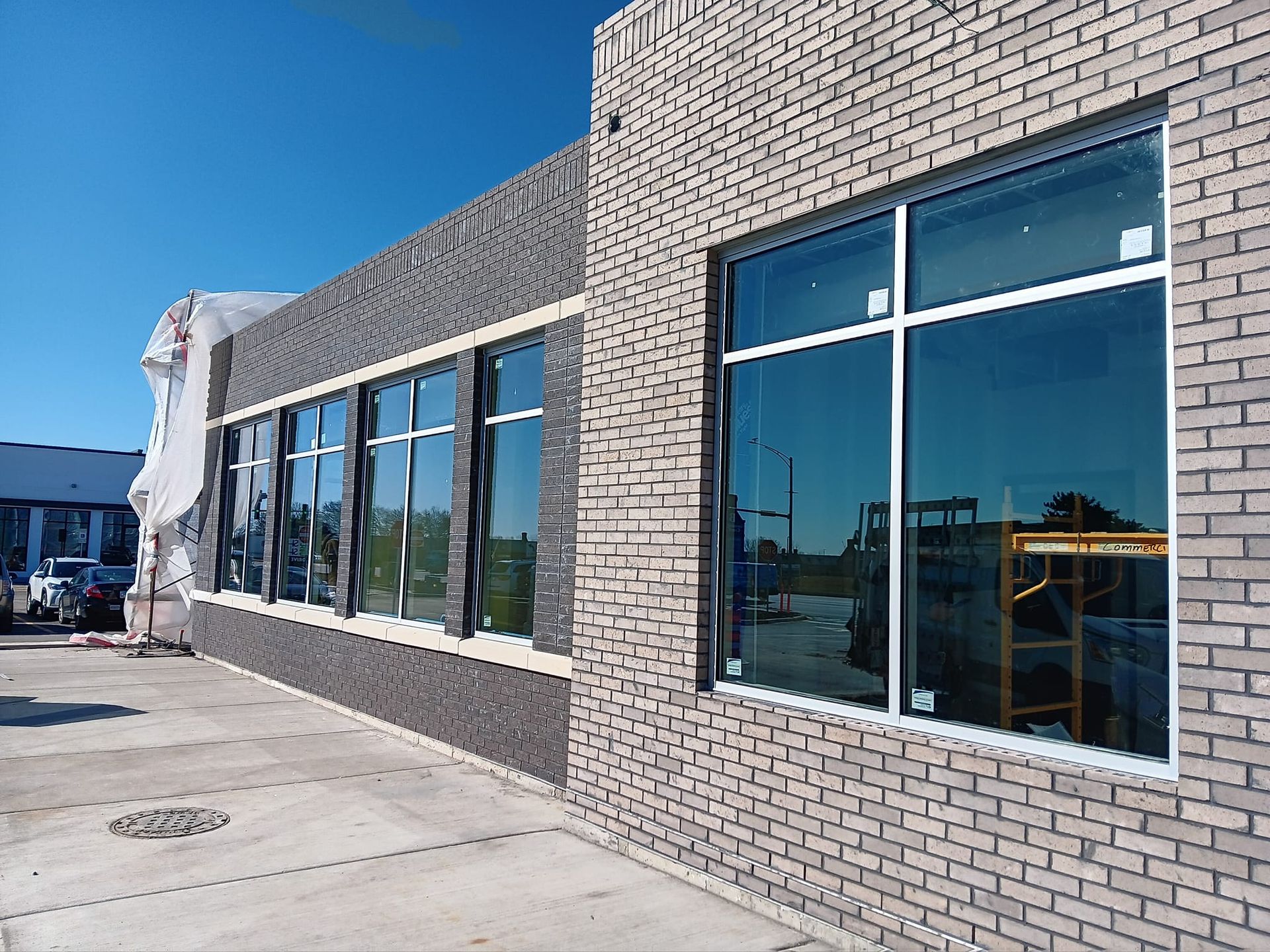 Building exterior with brick walls and large windows reflecting the sky and construction elements.