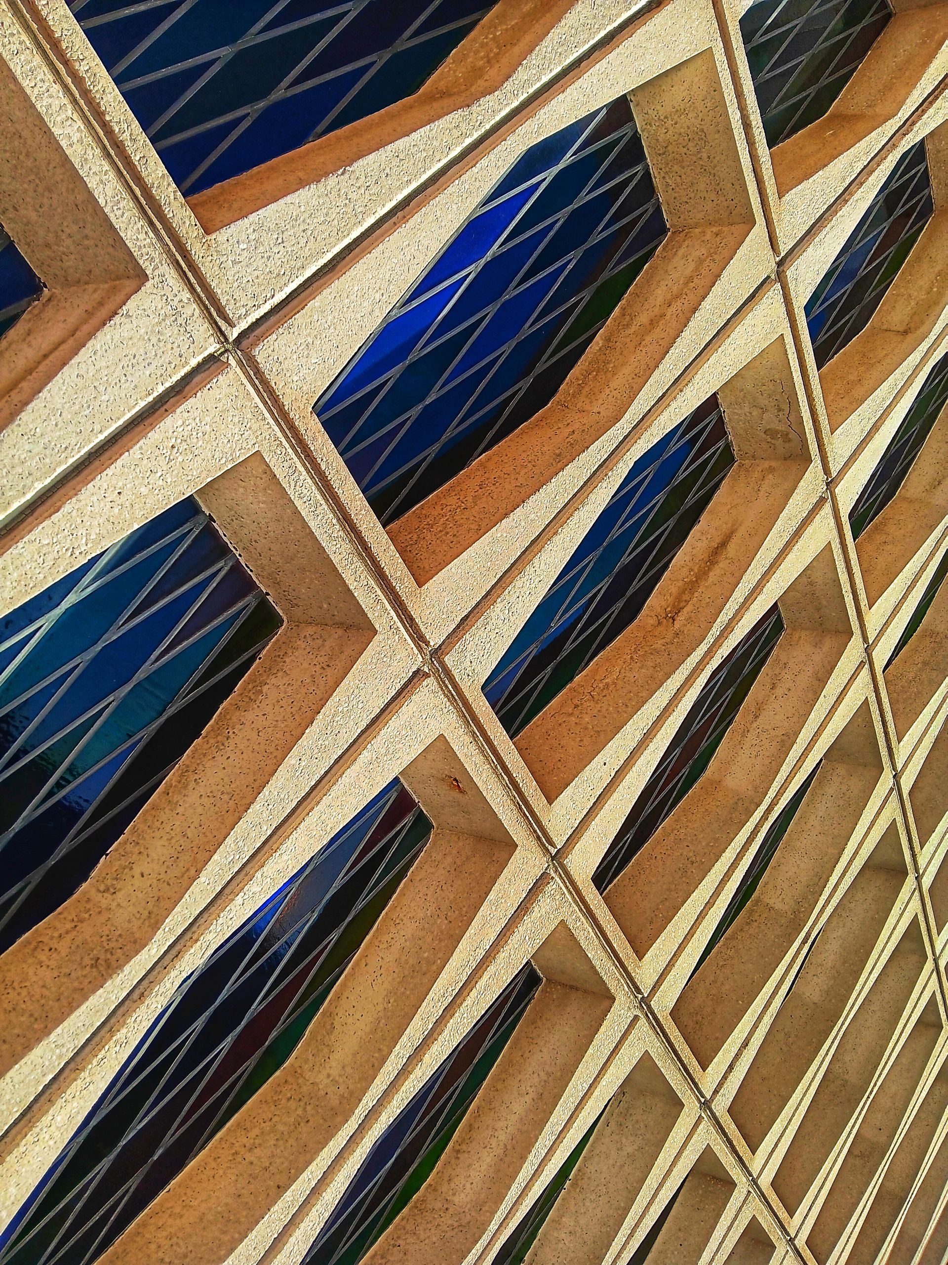 Diagonal view of a building's patterned windows; brown frames with dark blue and green diamond-patterned glass.