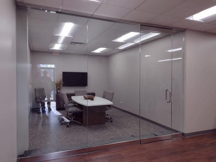 Glass-walled office: conference table, chairs, TV, and frosted privacy film on a wall.