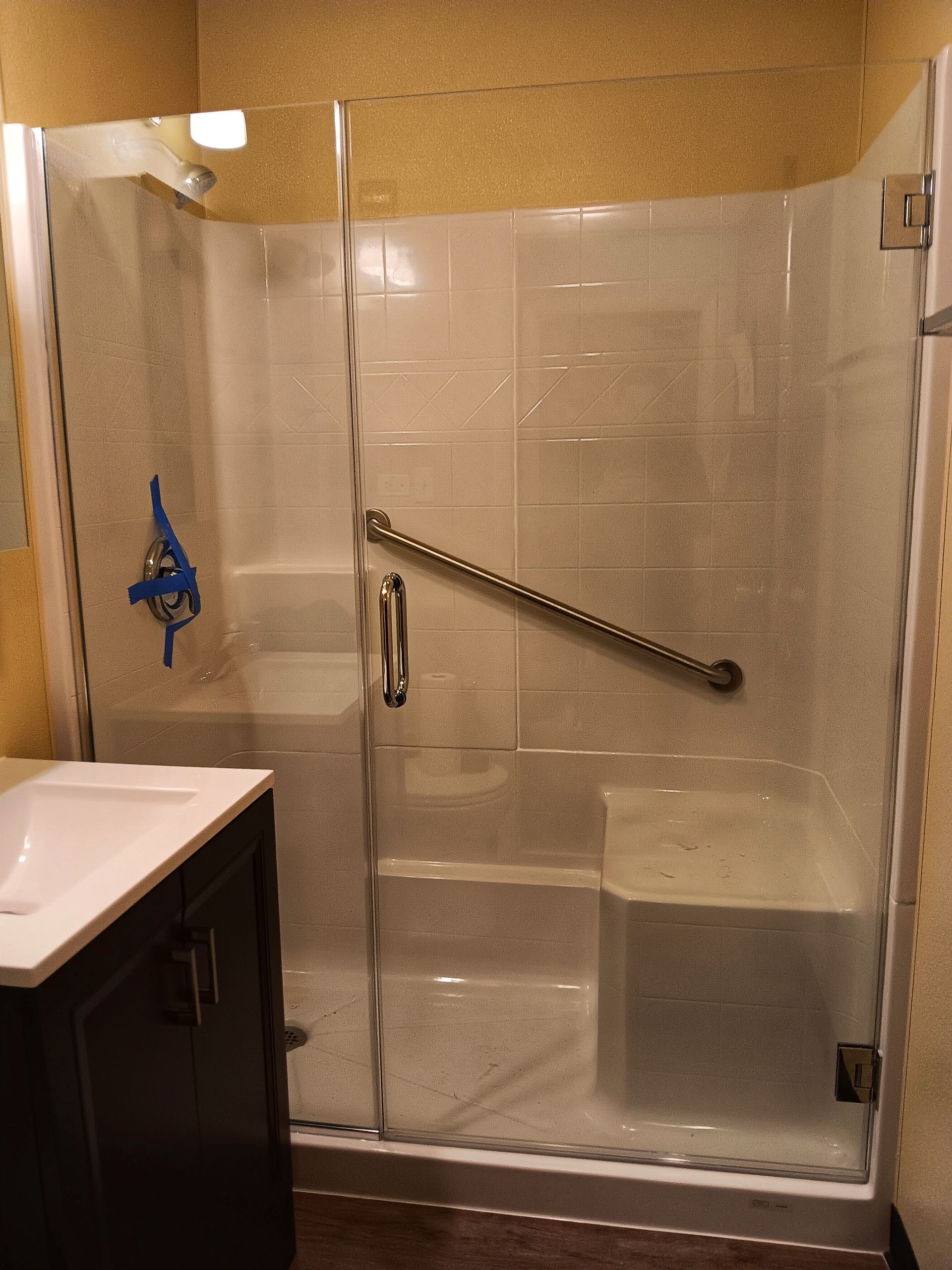 Shower stall with glass doors, a grab bar, and a built-in seat. A blue towel hangs inside.