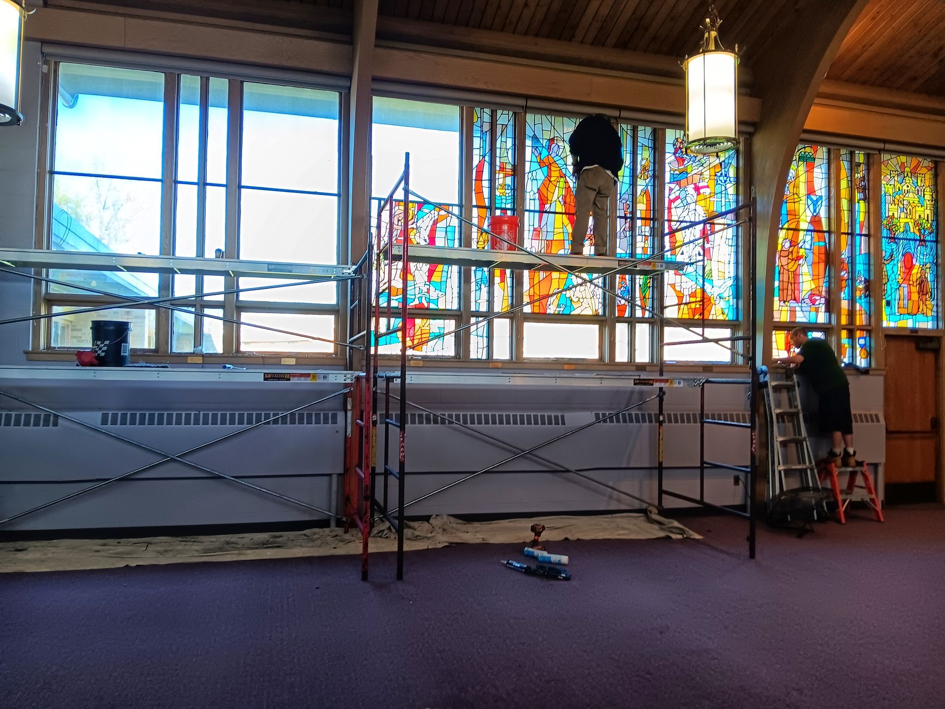 Two workers on scaffolding repair stained-glass windows in a church.