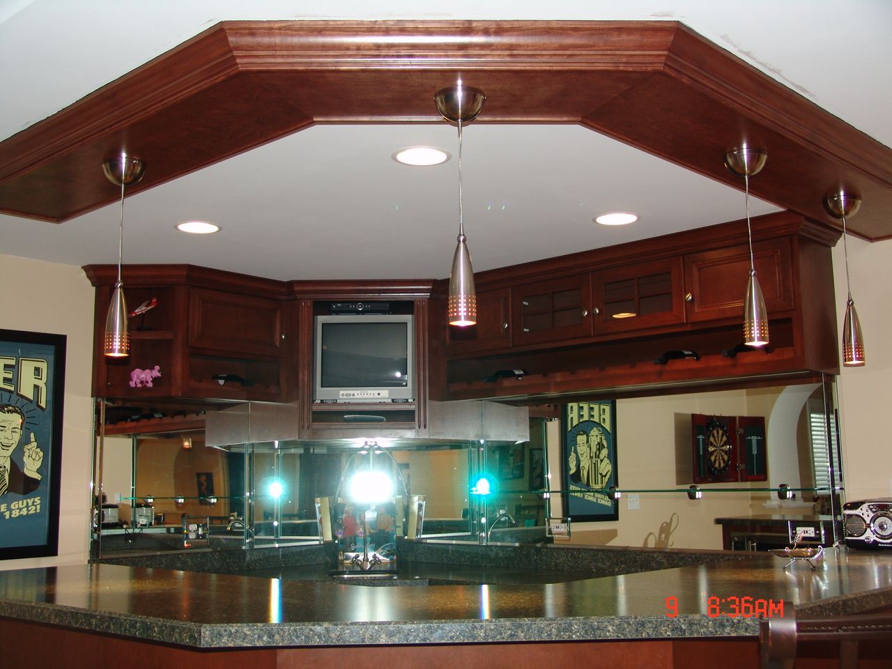 Dark wood home bar with countertop, mirrors, TV, overhead lights.