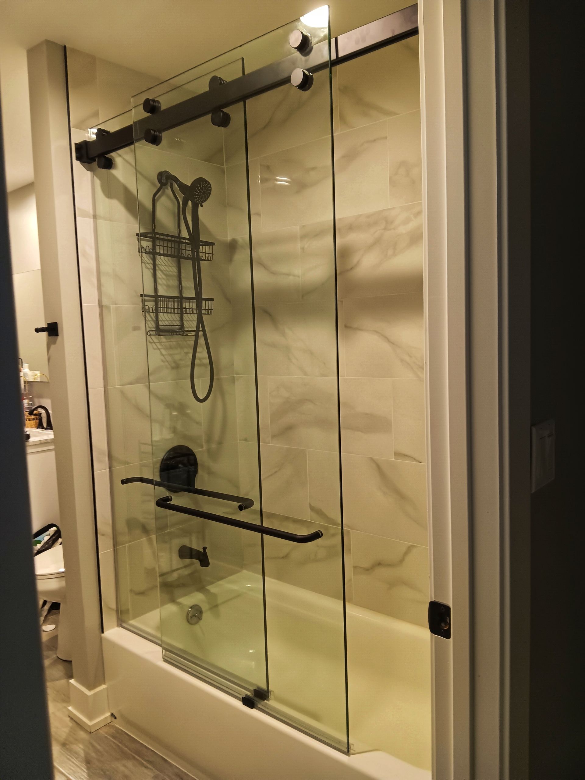 Modern shower with sliding glass doors, black hardware, and marble-look tile.
