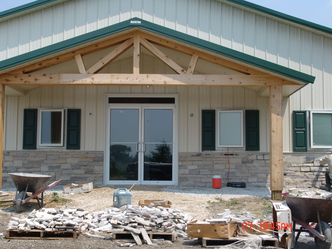 Exterior of a building with stone facade, glass doors, wooden porch, and construction materials.