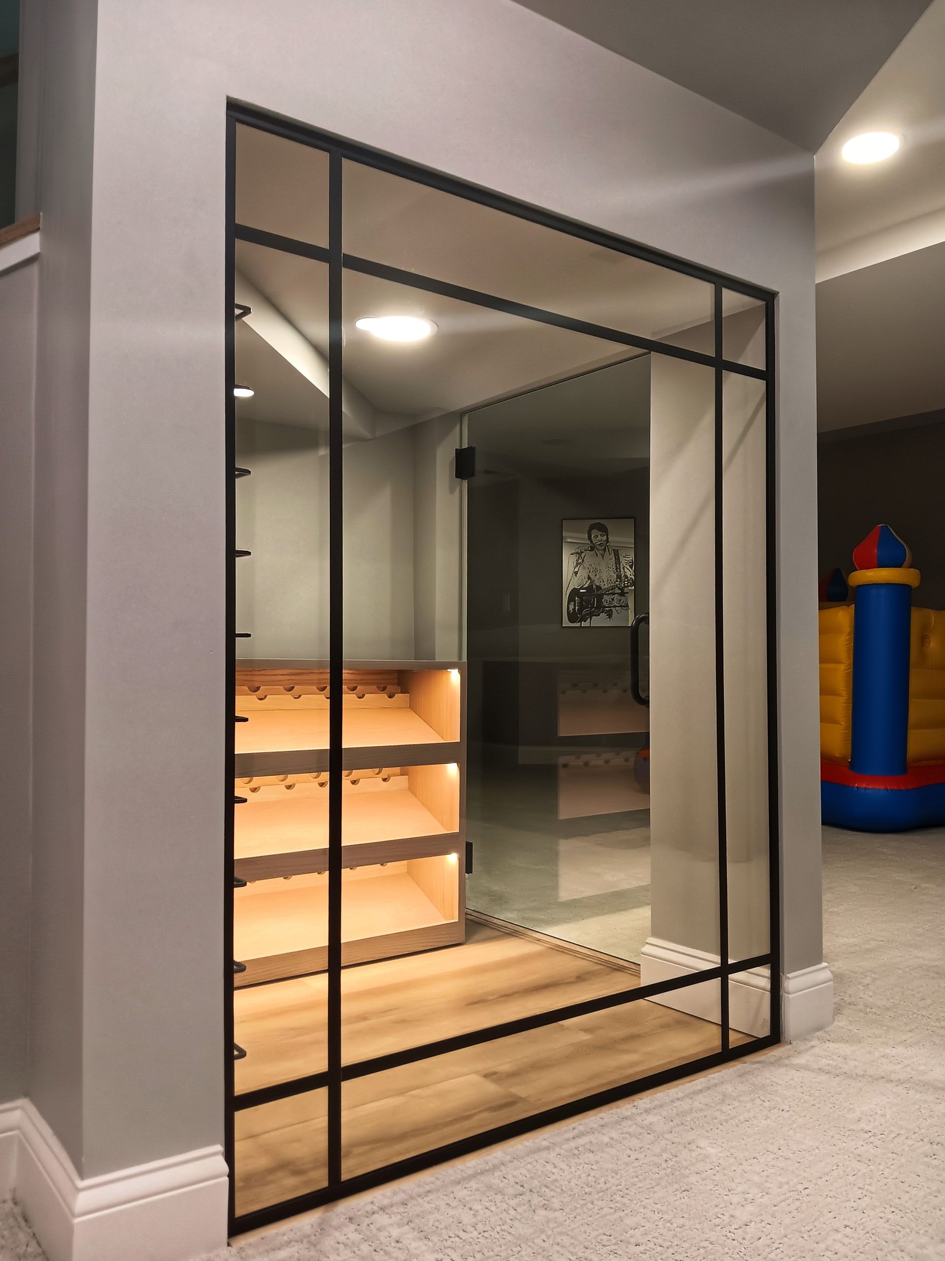 Glass enclosed play area with wooden steps and a black metal frame. A bouncy castle is in the background.