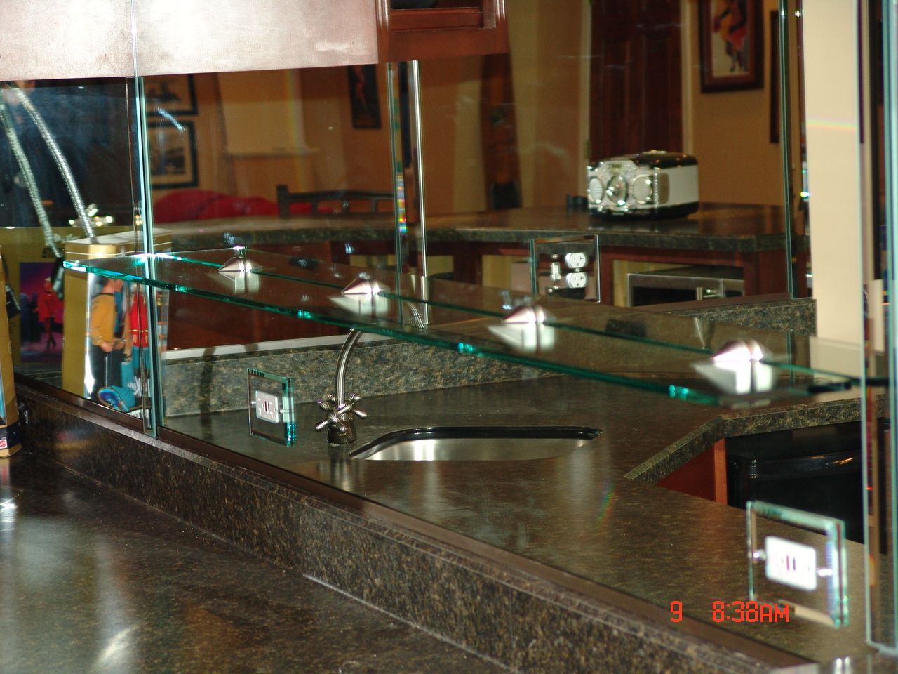 Bar area with granite counter, sink, and glass shelving. Mirror reflects the interior of the room.