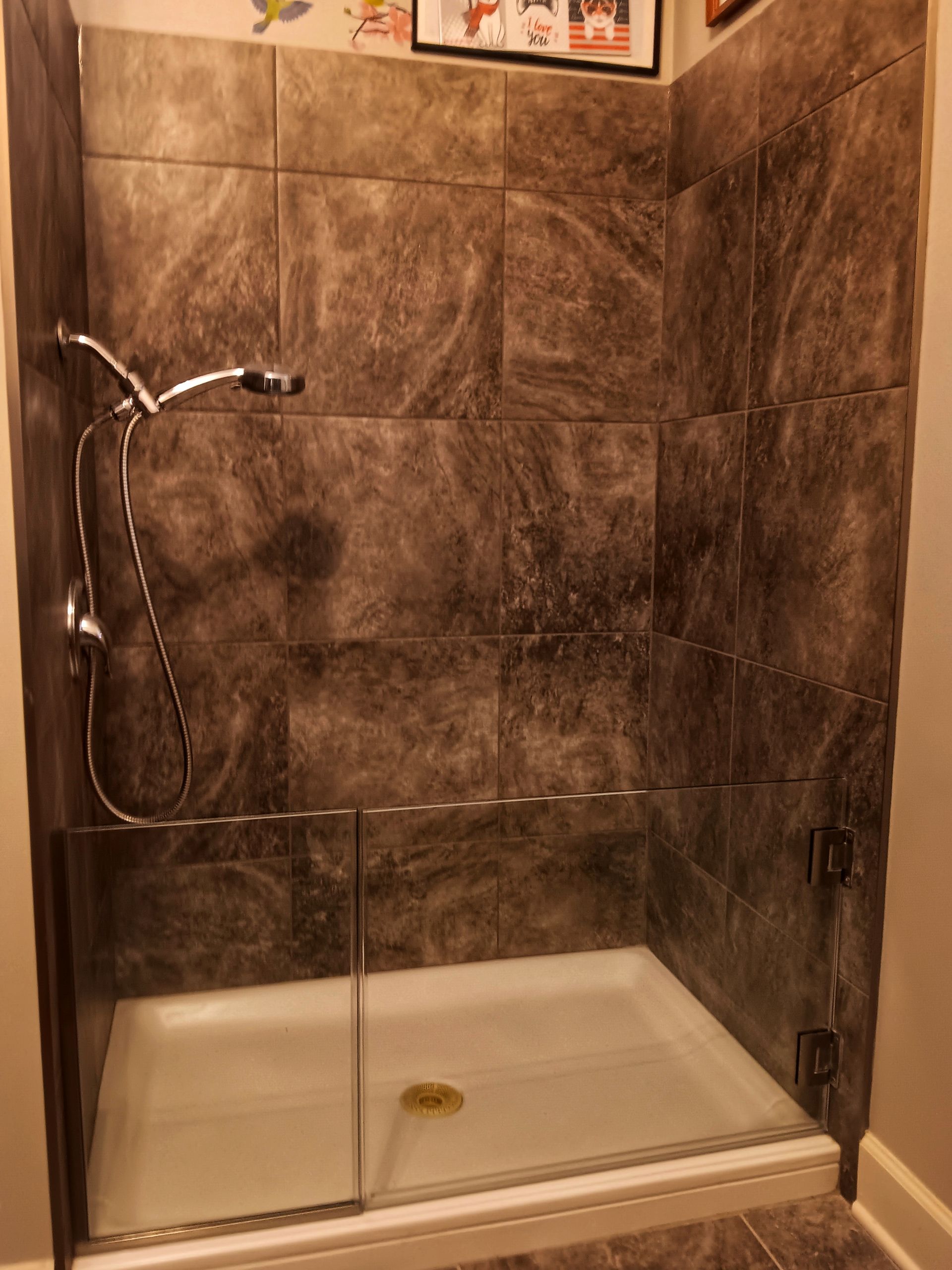 Shower with gray marbled tile walls, glass door, and white base.