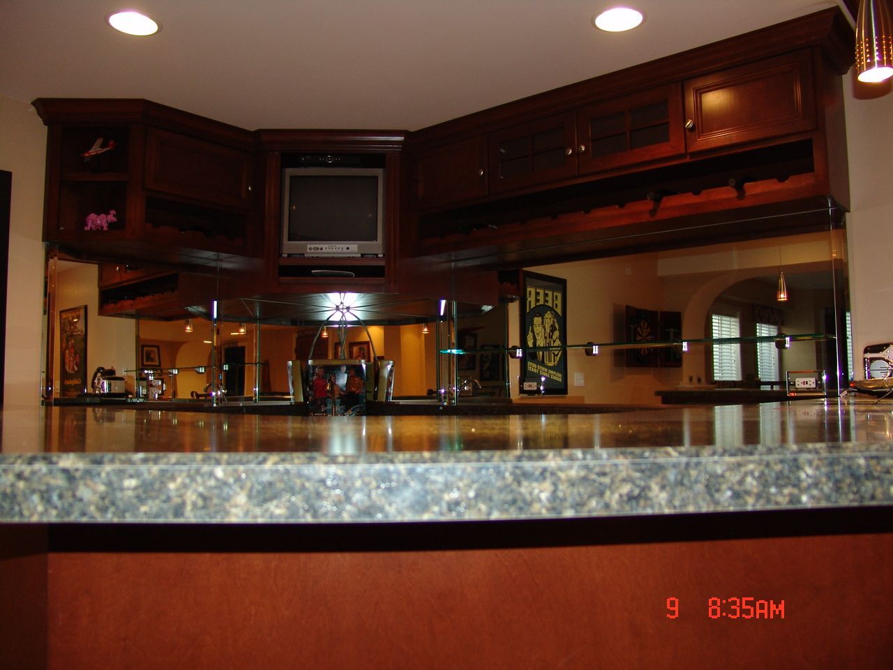 Dark wood bar with granite countertop, mirror backsplash, and cabinets. TV and beer signs visible.