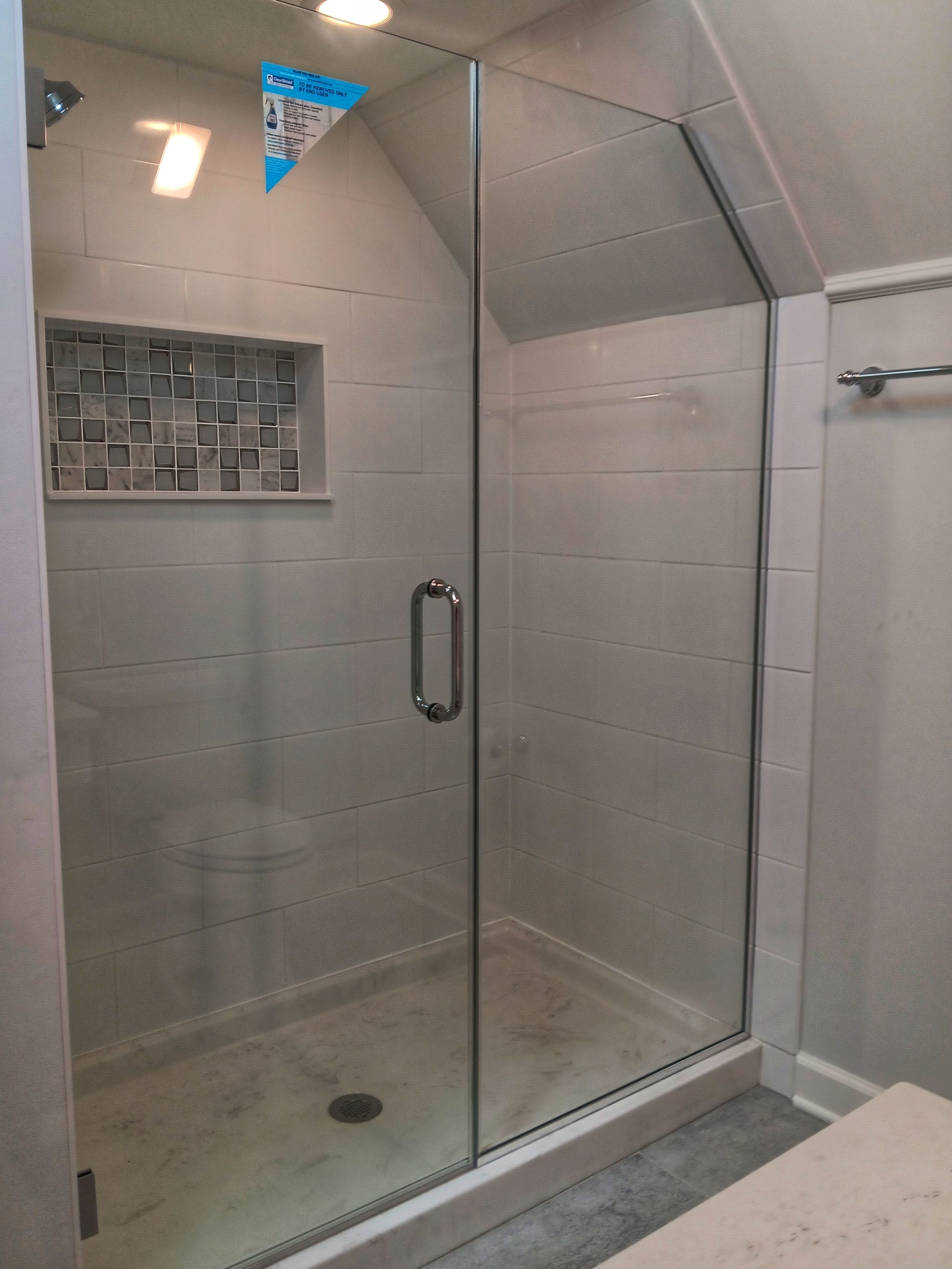 Glass shower enclosure with angled top, built-in shelf, and silver hardware in a bathroom.