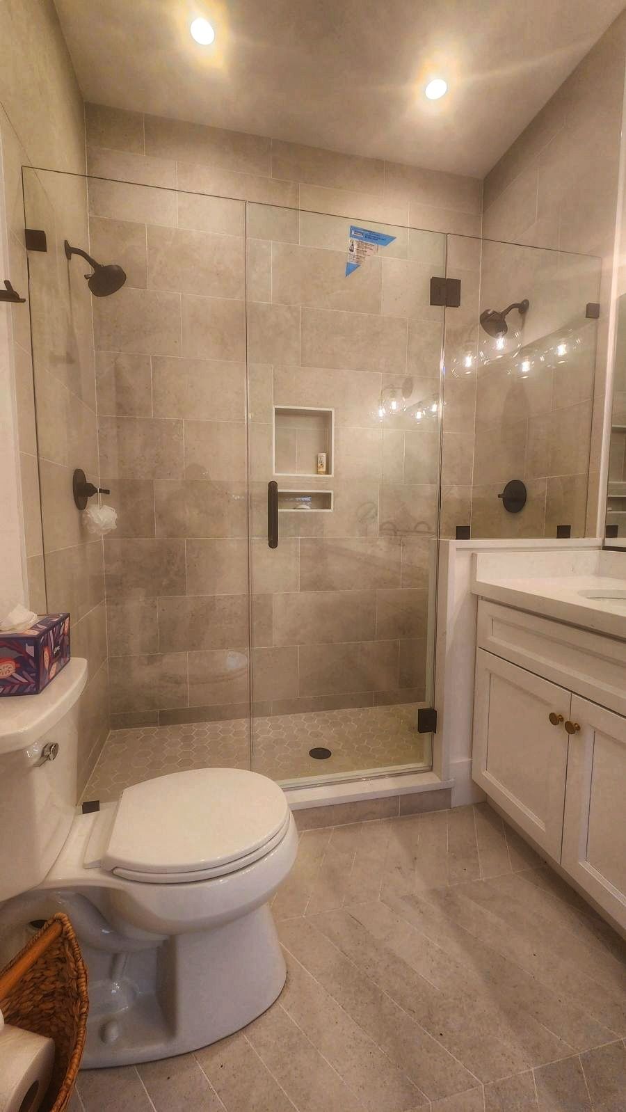 Bathroom with gray tile, glass shower, white vanity and toilet, dark hardware.