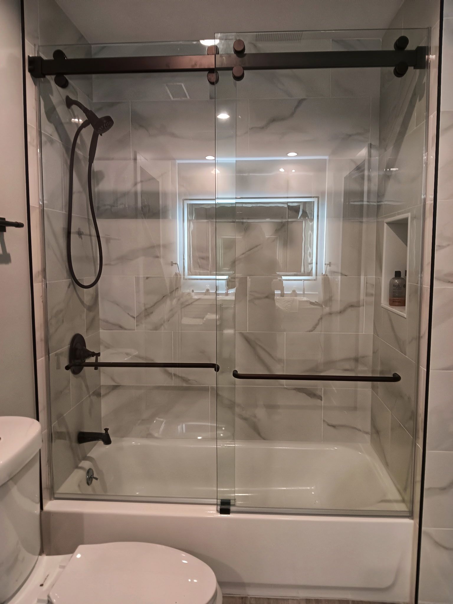 Glass shower door with dark fixtures over a bathtub in a modern bathroom.