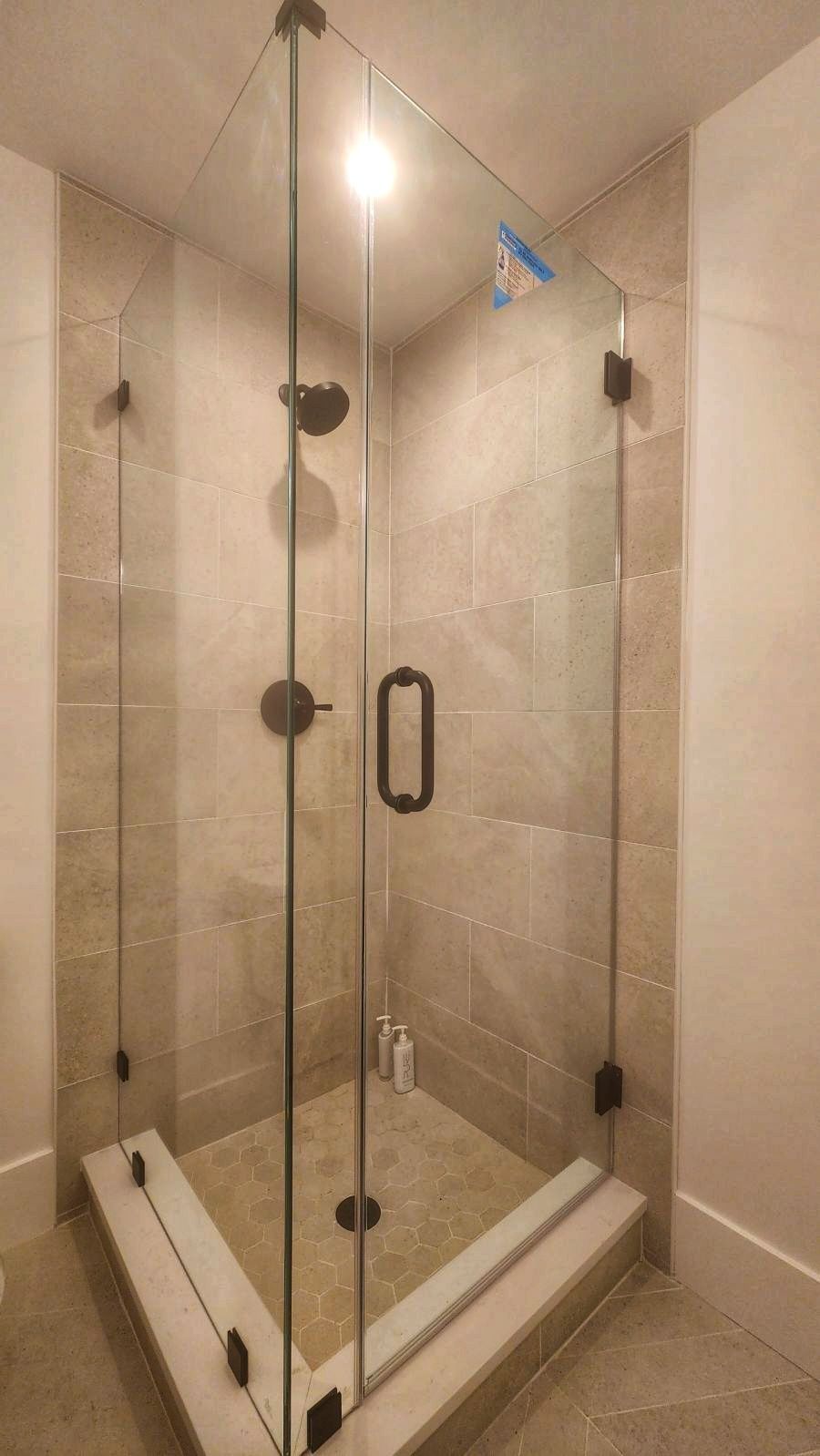 Corner glass shower with dark hardware, beige tile walls, and a light-colored shower base.