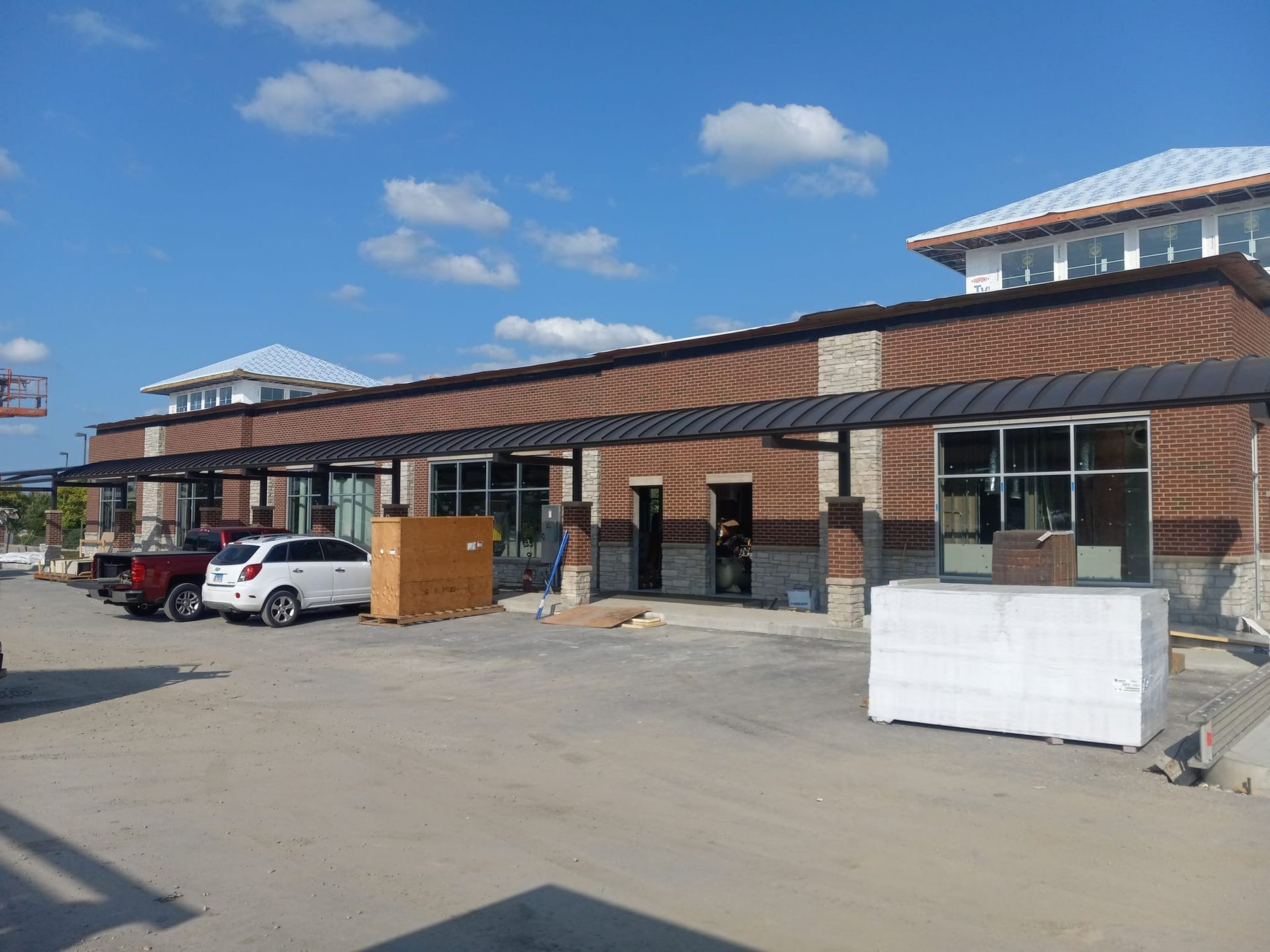 New construction: brick building with black awning, cars parked in front, clear blue sky.