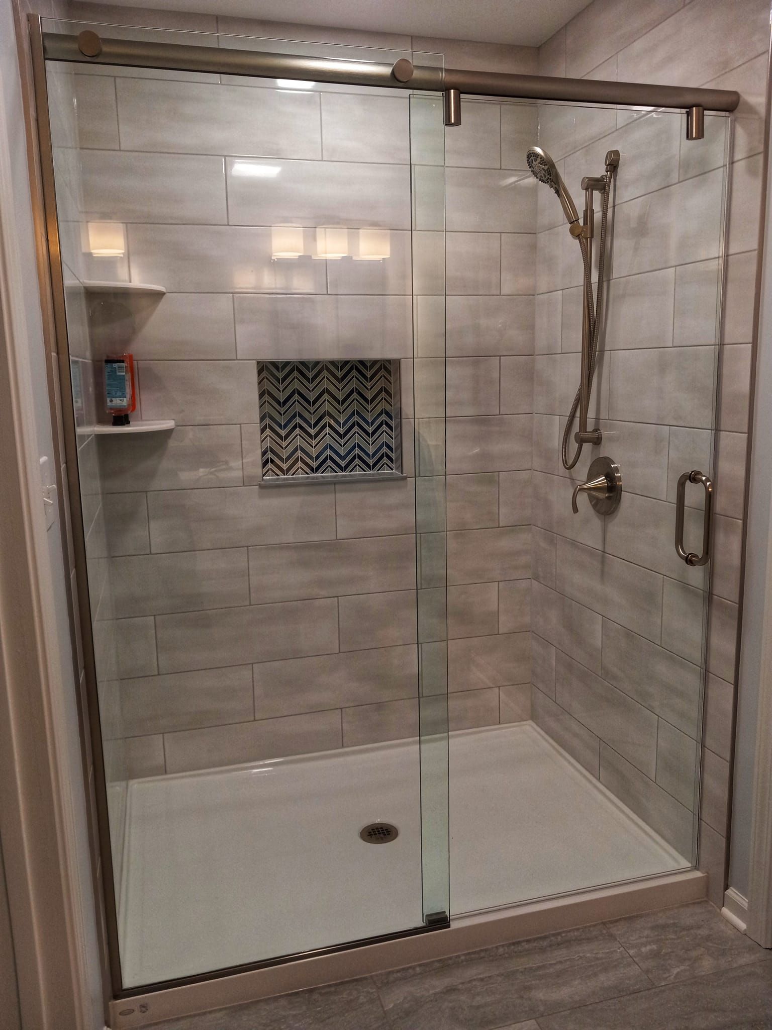 Modern glass shower with gray tile, a patterned niche, and chrome fixtures.