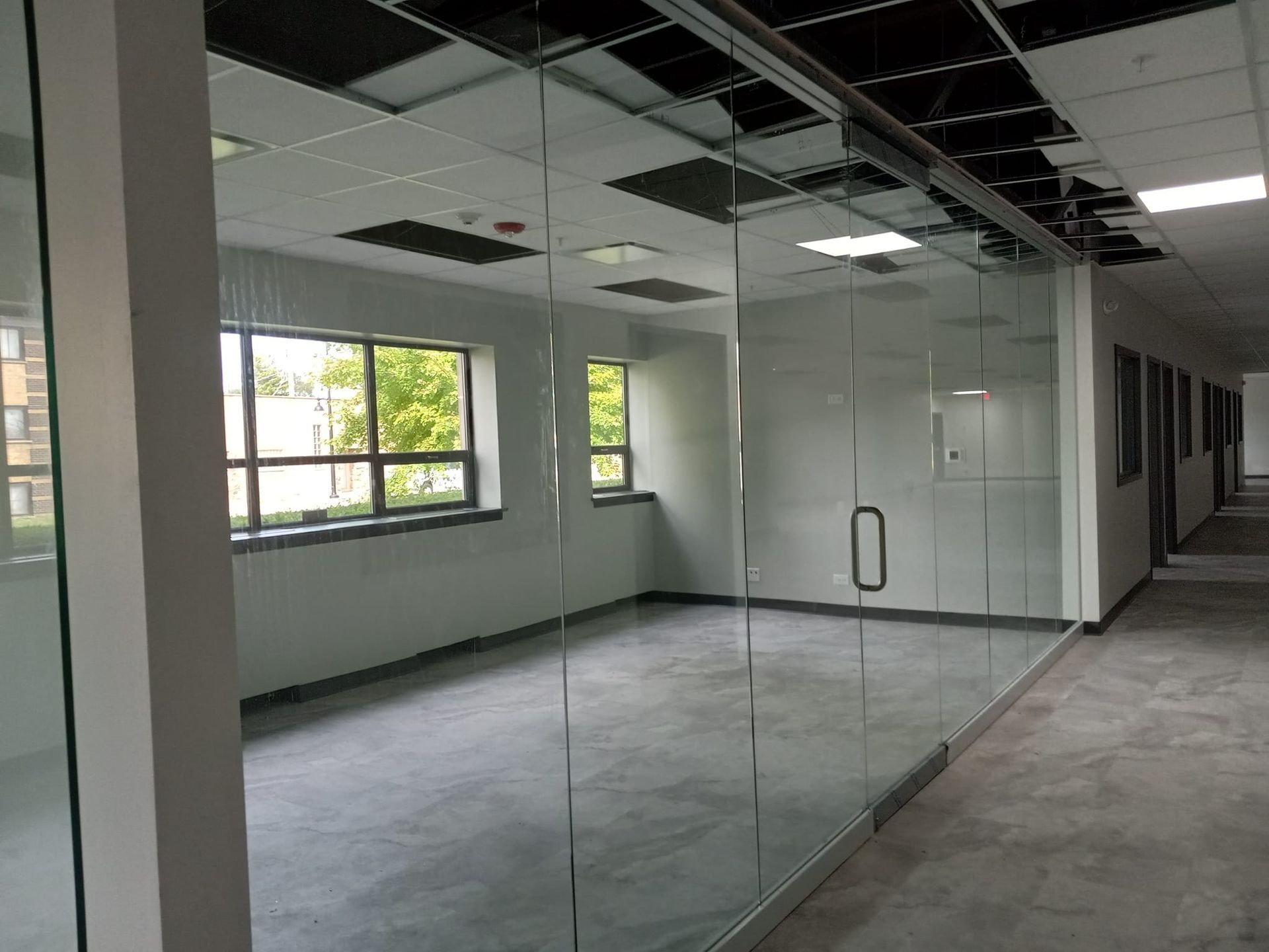 Empty office space with glass walls, windows, and a door, in a building hallway.