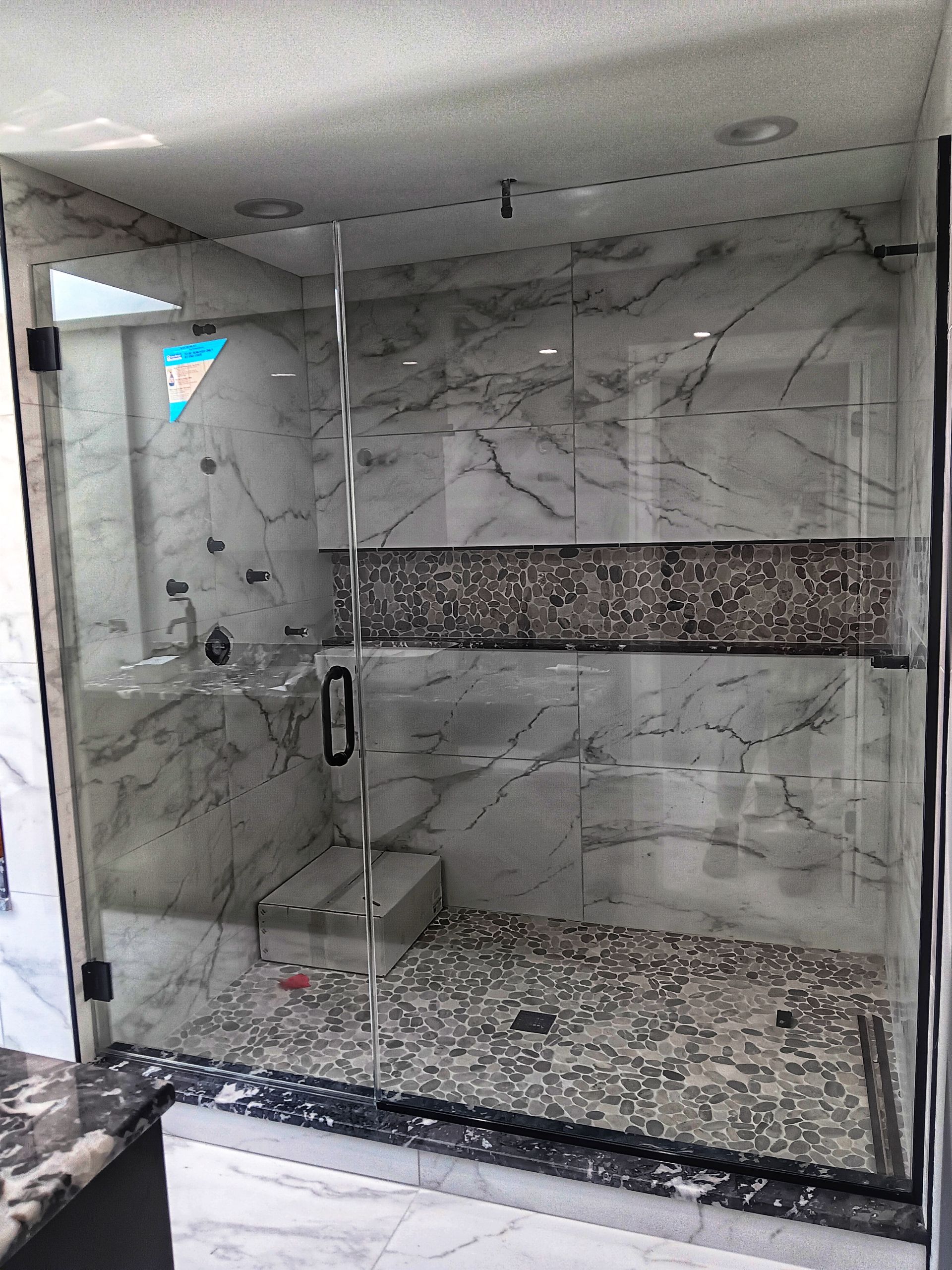 Glass shower with marble walls, mosaic floor, and a bench.