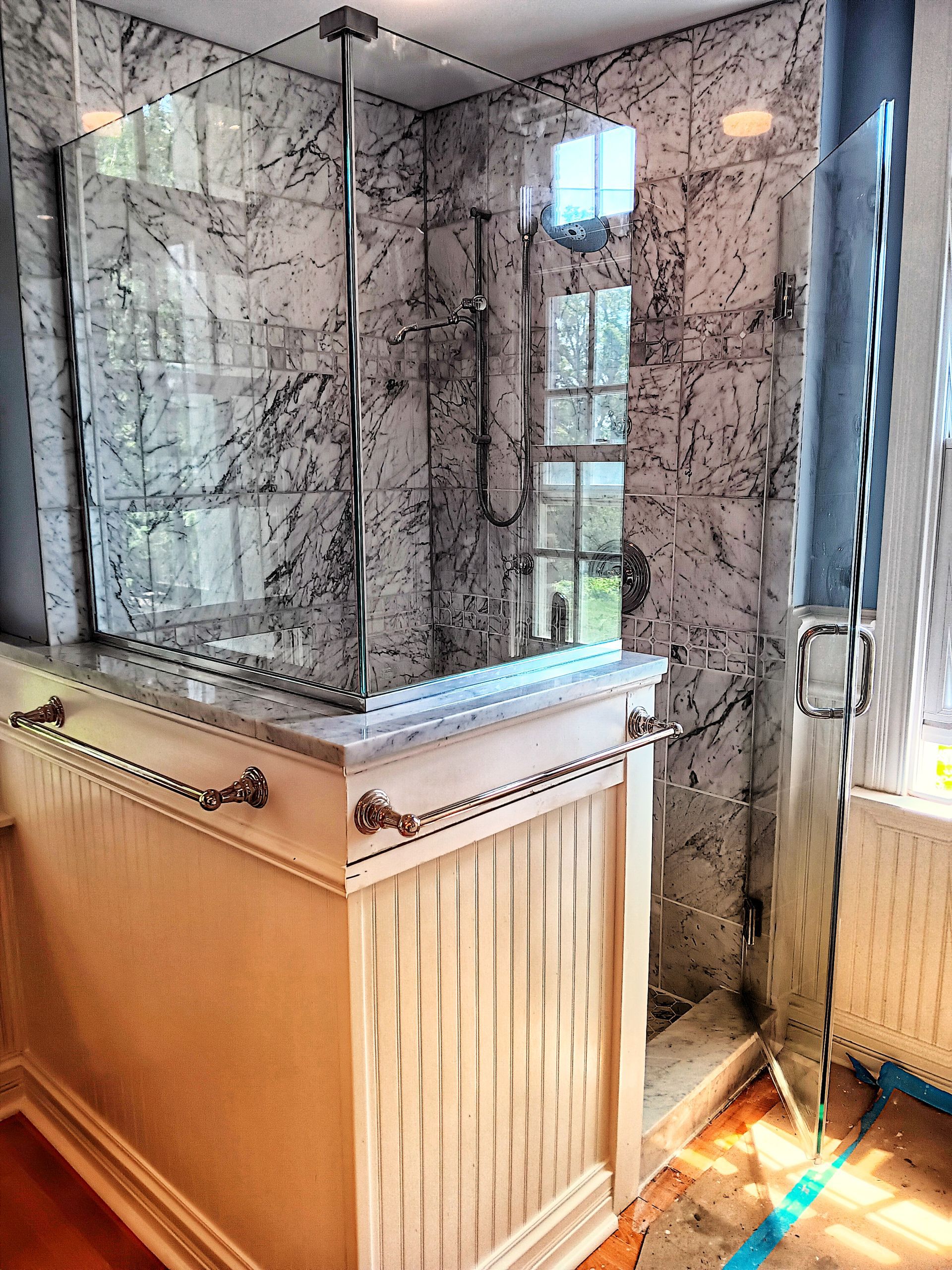Bathroom with marble shower, glass door, and white wainscoting.